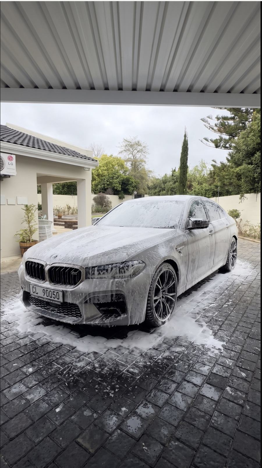 Silver BMW M5 covered in thick snow foam on a driveway